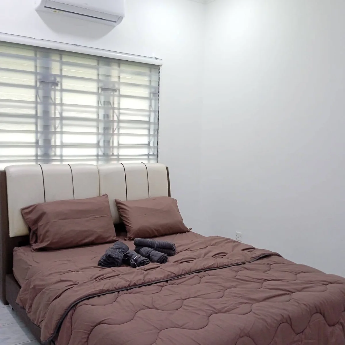 A neatly made bed beneath a window with blinds at Paradise Lodge