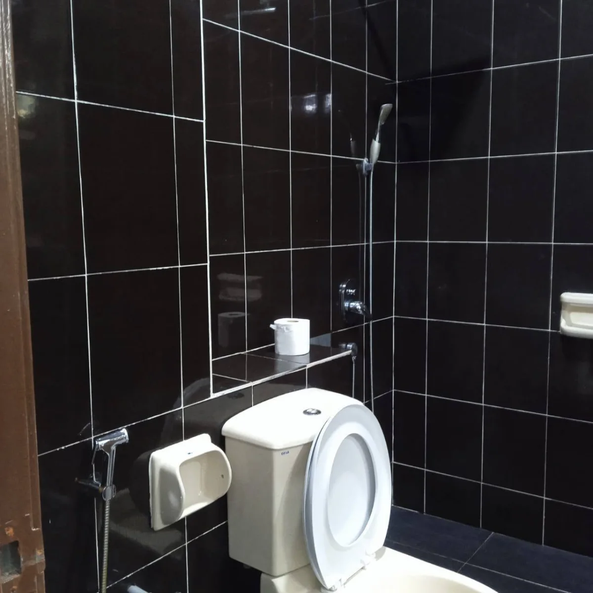 Toilet and handheld spray against black bathroom tiles at Paradise Lodge