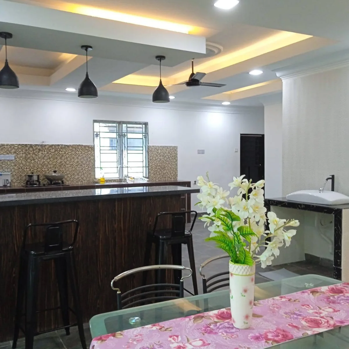 Kitchen counter, pendant lights and a dining table with flowers at Paradise Lodge